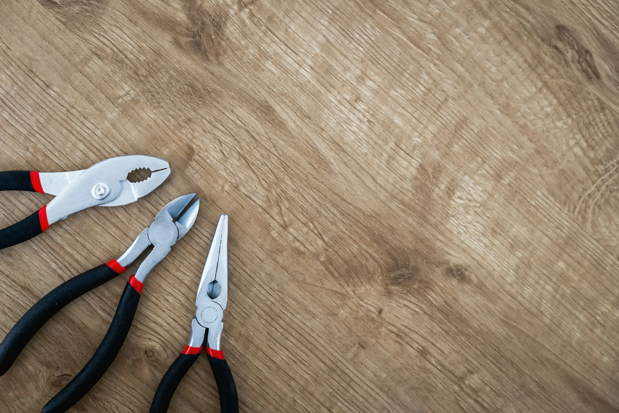 Pliers and electrician hand tools laid out on a wooden surface