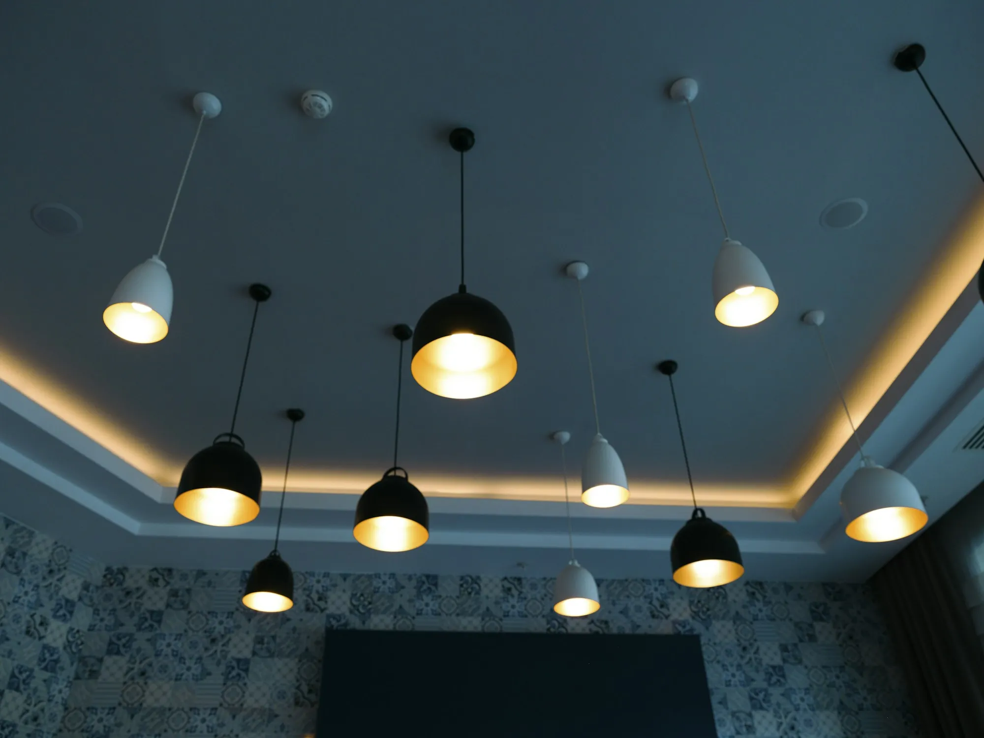 Dark kitchen ceiling with a row of black pendant lights and a warm cove glow