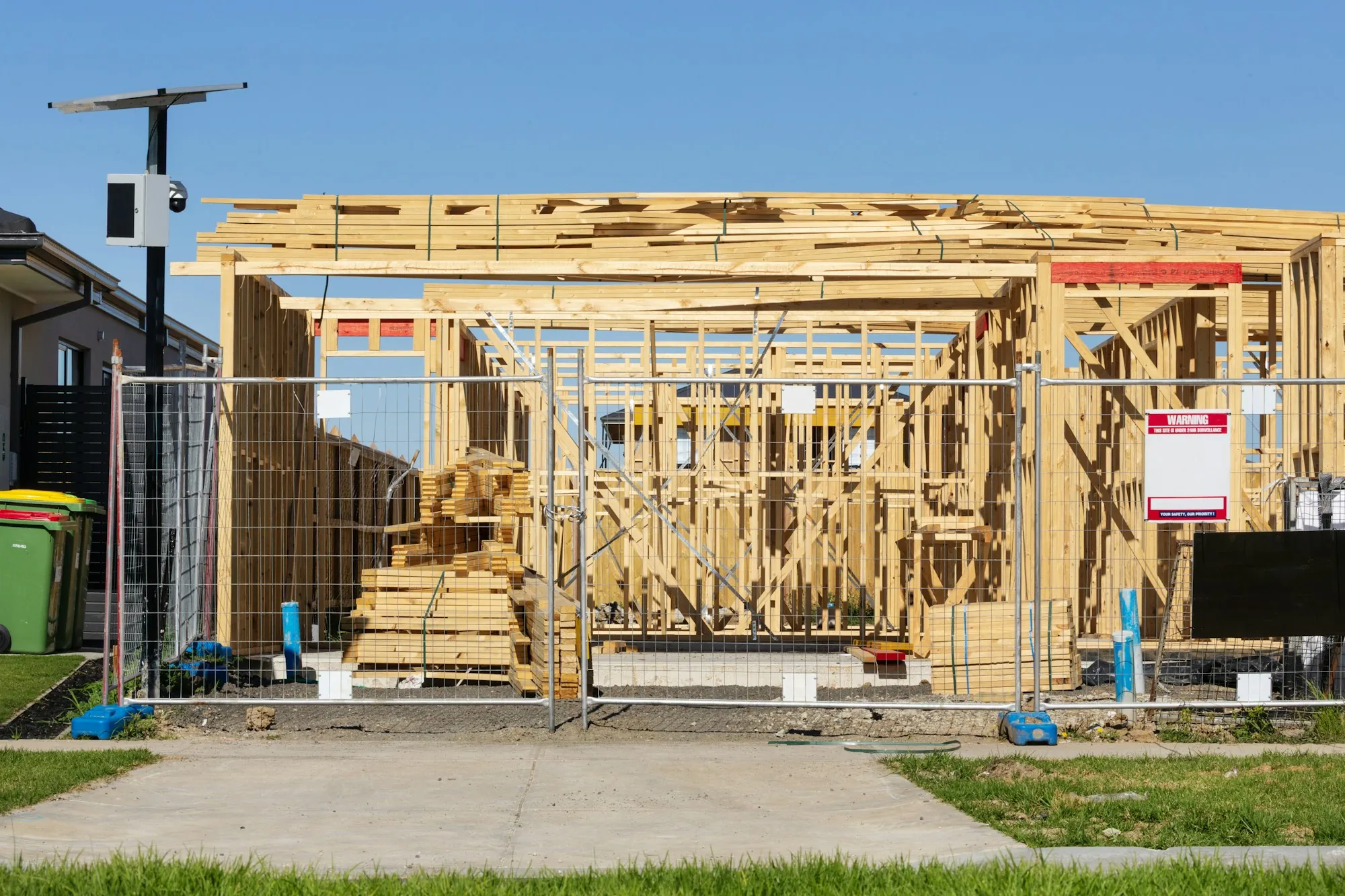 New timber-framed house under construction behind a site fence